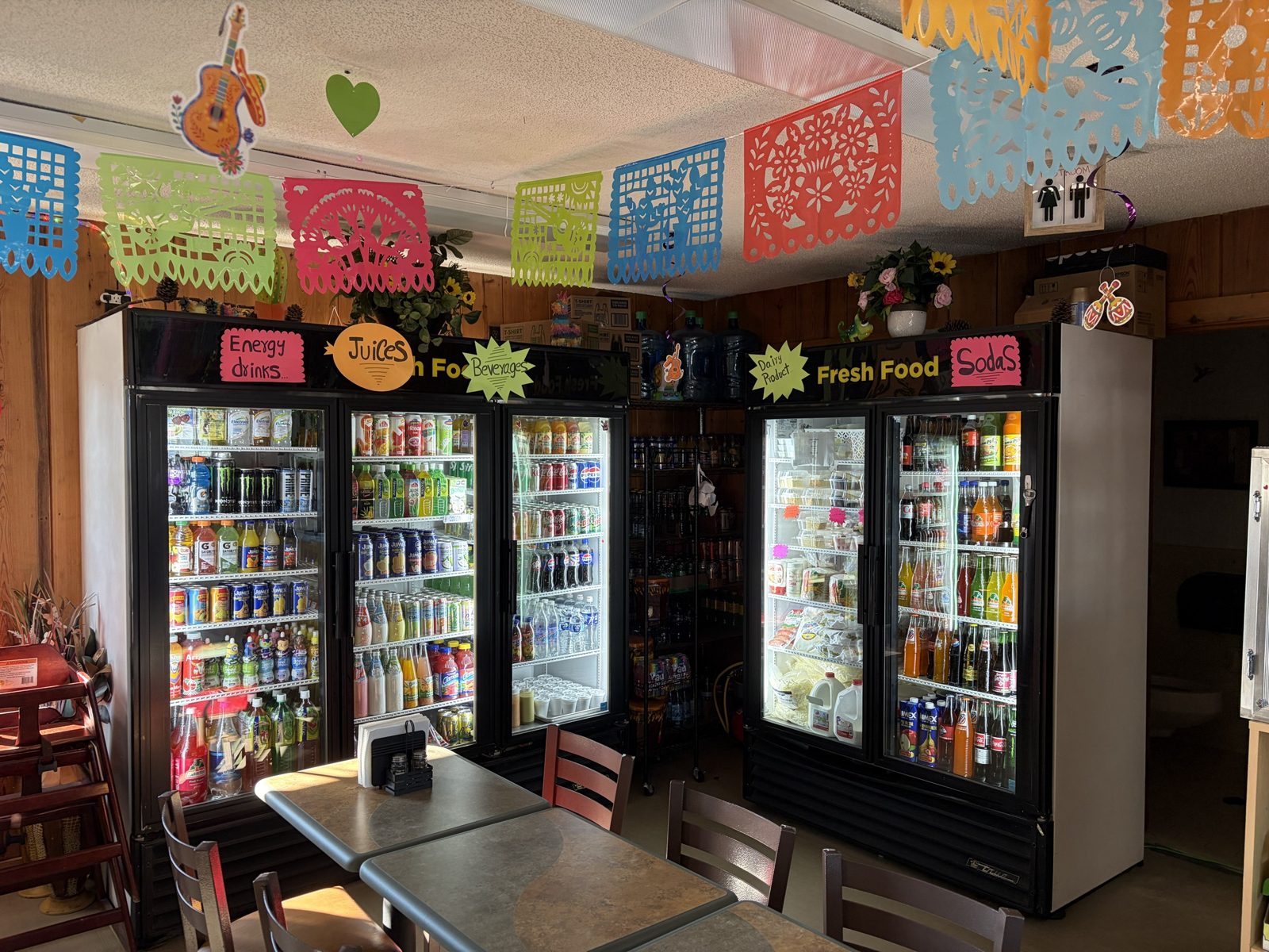 Inside the store: cases of drinks and juices with papel picado hanging overhead, and dining tables in front